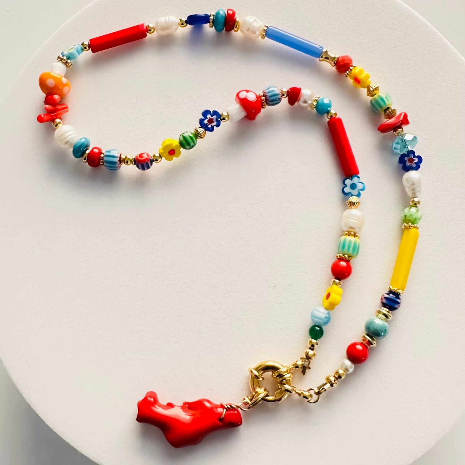 Embrace the vibrant essence of summer with our enchanting necklace, a playful symphony of colors and textures. This unique piece features a delightful mix of Millefiori beads, pearls, evil-eye beads, corals, glass beads, bamboo chips, Murano crystals, and ceramics. Adorned with dainty Millefiori flowers and charming Murano mushrooms, it exudes a whimsical, childlike joy. The multicolored beads create a captivating mosaic of hues, making this necklace a wearable celebration of life. Secured with a marine gold clasp, this lively accessory is perfect for adding a splash of color and a touch of fun to any outfit. Let its lively colors and intricate details bring a sense of joy and carefree elegance to your style.
