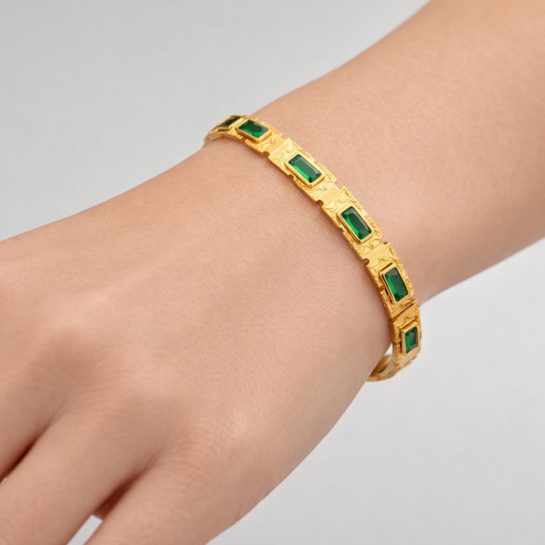 Gold-tone stainless steel bangle with emerald-green zirconia worn on a woman’s hand.